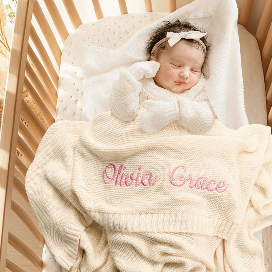 Newborn asleep under a knitted blanket embroidered with the name Olivia Grace